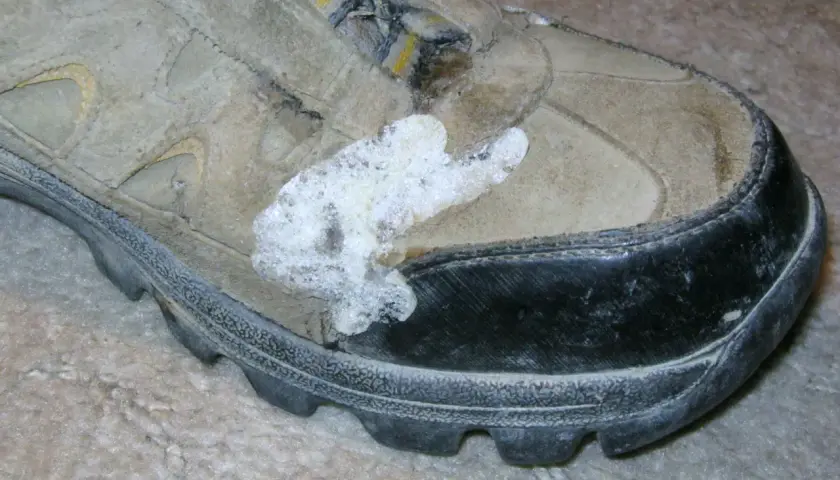 A dirty hiking boot with a white, foamy substance stuck to the side, possibly from a failed attempt to schuhsohle kleben (glue the shoe sole).