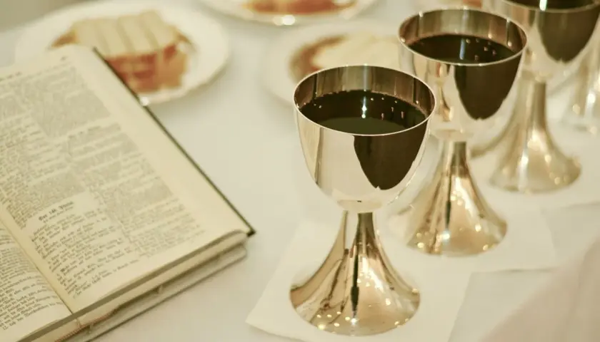 Ein offenes Buch liegt neben silbernen Kelchen, gefüllt mit dunklem Wein. Vielleicht bereitet Konrad Krajewski eine Feier vor.