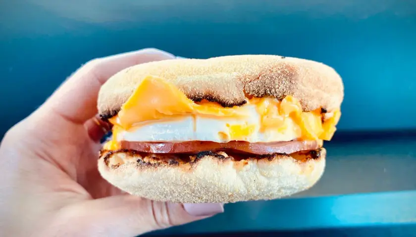 Mcmuffin farmerski z jajkiem sadzonym, plastrem szynki i roztopionym serem, trzymany w dłoni.