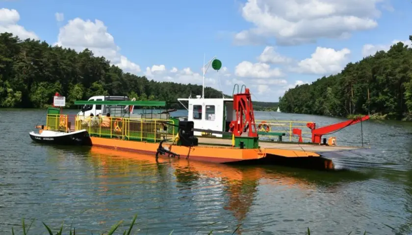 Prom na Zalewie Prężyce z białym vanem i pomarańczowym pokładem, otoczony zielonymi lasami.