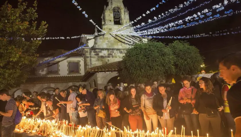 Multitud enciendiendo velas frente a una iglesia iluminada por guirnaldas, parte de las fiestas de Revilla de Camargo.