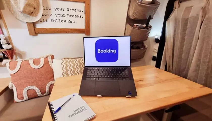 Laptop con app Booking aperta, pronto per un **instant booking** di avventure. Taccuino "Happy Thoughts" accanto.