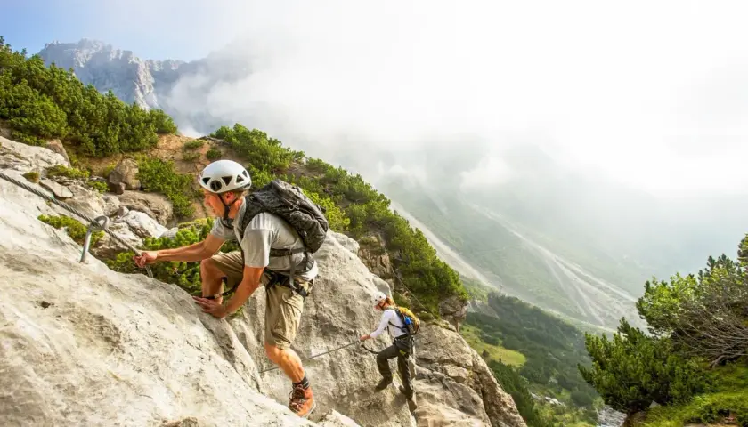 Dwóch turystów pokonuje via ferrata w Austrii, wspinając się po skalnej ścianie z ubezpieczeniem stalowej liny.