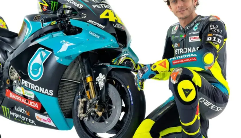 Valentino Rossi posa junto a su moto de competición, luciendo su icónico traje de carreras.