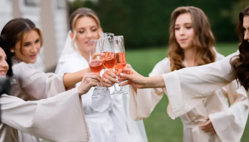Cinq femmes portent des robes de chambre en soie et portent des verres de champagne rosé pour un vin d'honneur à 16h.