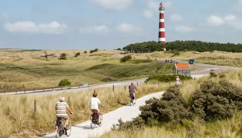 Ciclistas disfrutan de un paseo por la ruta EuroVelo 7, con un faro a rayas rojas y blancas al fondo.