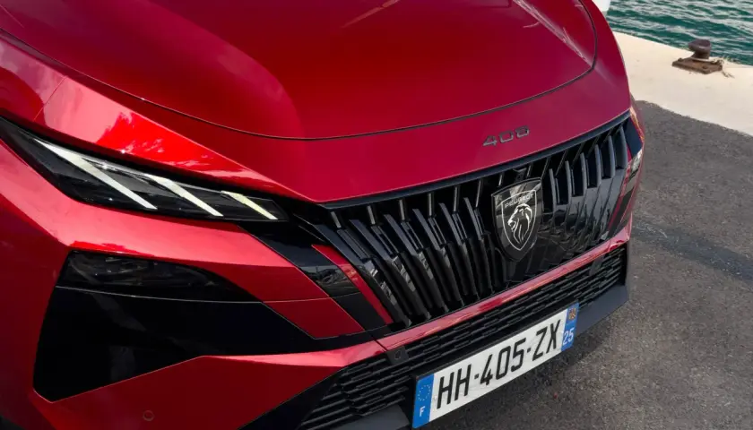 Czerwony Peugeot 408 Hybrid z charakterystycznym grillem i ostrymi światłami LED, gotowy do podróży nad wodę.