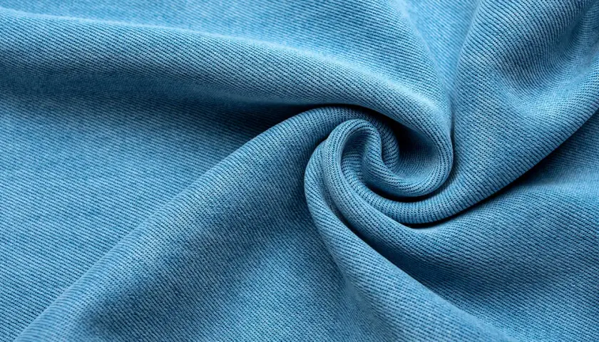 Miękka, błękitna tkanina lyocellu z charakterystycznym splotem, ułożona w eleganckie fale i spiralę.