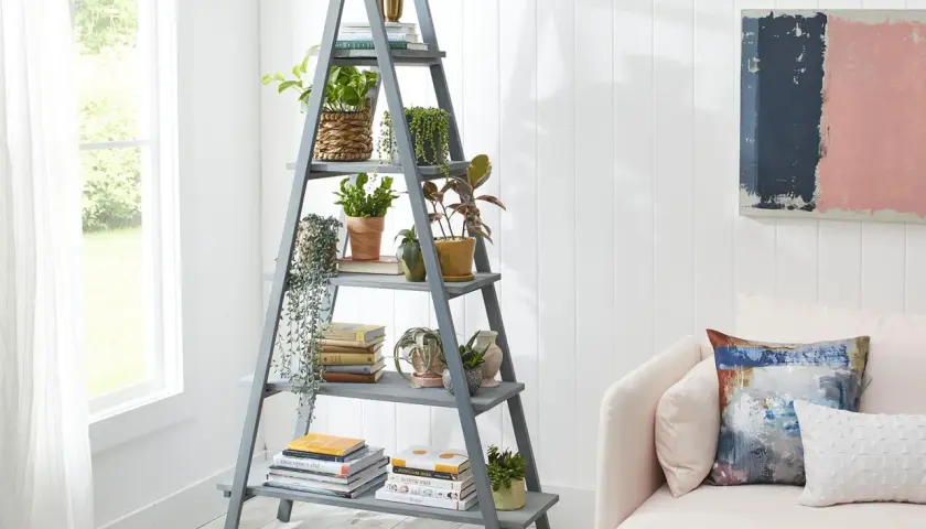 Perchero escalera gris con plantas y libros, junto a un sofá rosa.