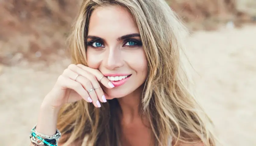 Blondynka o niebieskich oczach, zmysłowo uśmiechnięta. Idealne kolory ubrań dla blondynek o niebieskich oczach podkreślą jej urodę.