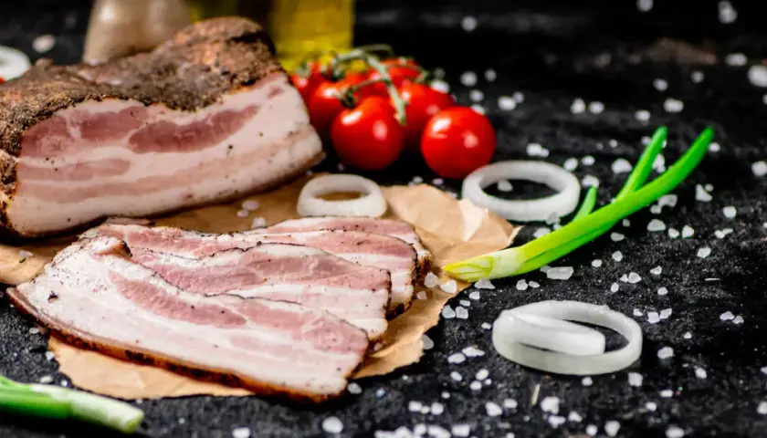 Idealny boczek do carbonary: plastry wędzonego boczku, pomidorki, cebula i szczypiorek na czarnym tle.