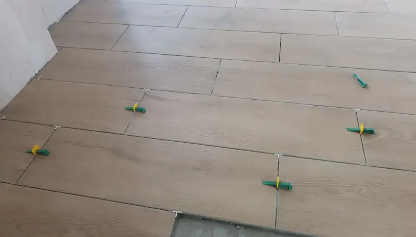 Posa di piastrelle effetto legno con distanziatori verdi. Ottenere preventivi per i prezzi piastrellista al mq è fondamentale per un lavoro ben fatto.