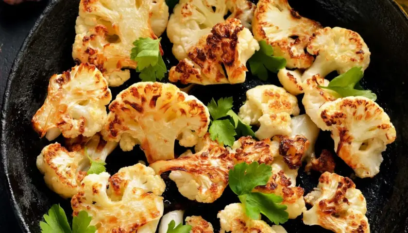 Chou-fleur rôti au four, doré et caramélisé, garni de persil frais dans une poêle en fonte. Un délice croustillant.