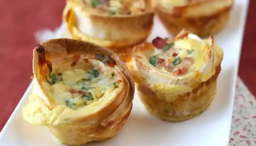 Petits quiches wraps dorés, garnis d'œufs, de lardons et de persil, servis sur une assiette blanche.