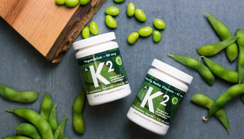 Zwei Flaschen Vitamin K2, umgeben von frischen Edamame-Bohnen. Vegane K2-Lebensmittel für gesunde Knochen.