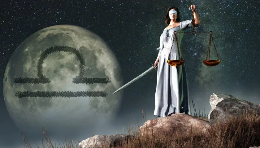 Kobieta z przepaską na oczach, trzymająca wagę i miecz, stoi na tle księżyca z symbolem Wagi. Ascendent w wadze.
