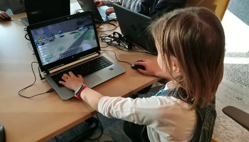 Dzieci grają w grę komputerową na laptopach podczas lekcji kodowania.