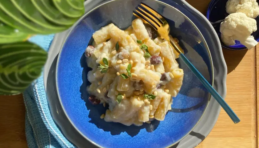 Piatto di pasta e cavolfiore cremoso, guarnito con pinoli e erbe aromatiche, pronto per essere gustato.