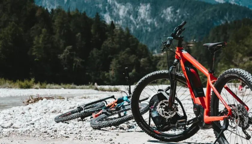 Aventura en Croacia en bicicleta, con bicicletas de montaña listas junto a un río pedregoso y un bosque frondoso.