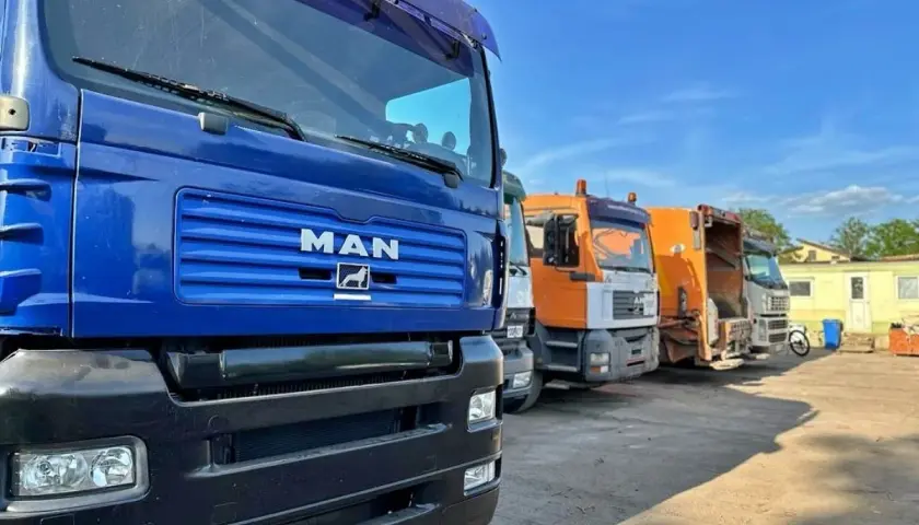 Rząd ciężarówek, w tym śmieciarek, gotowych do odbioru materiałów z recyklingu.