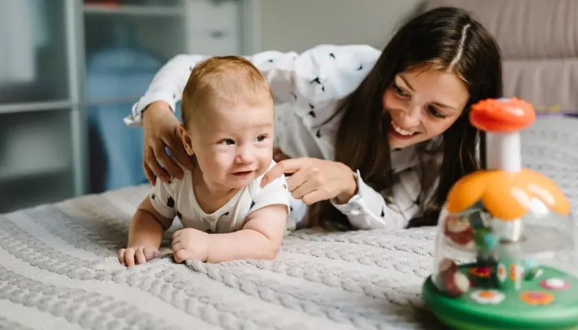Mamma incoraggia il suo neonato di 1 mese in una divertente attività sul lettone, con un giocattolo colorato.