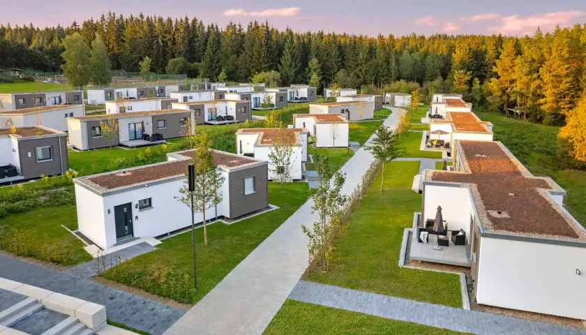 Reihe von kleinen Häusern, modern und minimalistisch, mit begrünten Dächern, eingebettet in eine grüne Landschaft am Waldrand.
