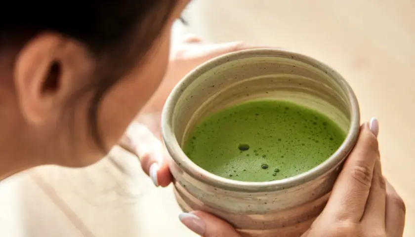 Frau hält eine Schale mit schaumigem, leuchtend grünem Matcha. Die ideale matcha temperatur für den perfekten Genuss.