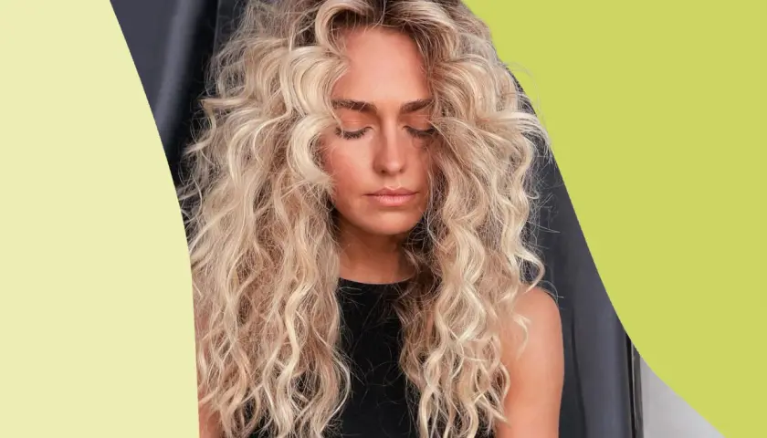 Mujer con cabello rubio, rizado y esponjoso, con los ojos cerrados y un ligero bronceado.