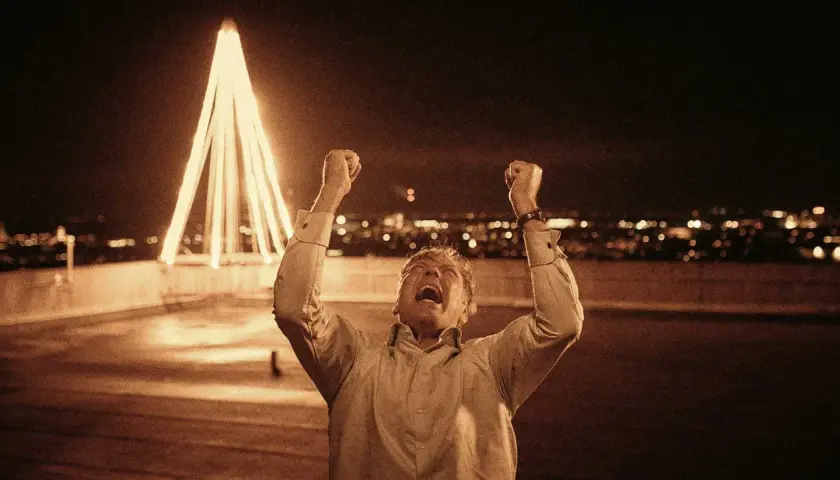 Man jublar med knutna nävar mot en upplyst julgran och stad i bakgrunden. Känslan av riket exodus infinner sig.