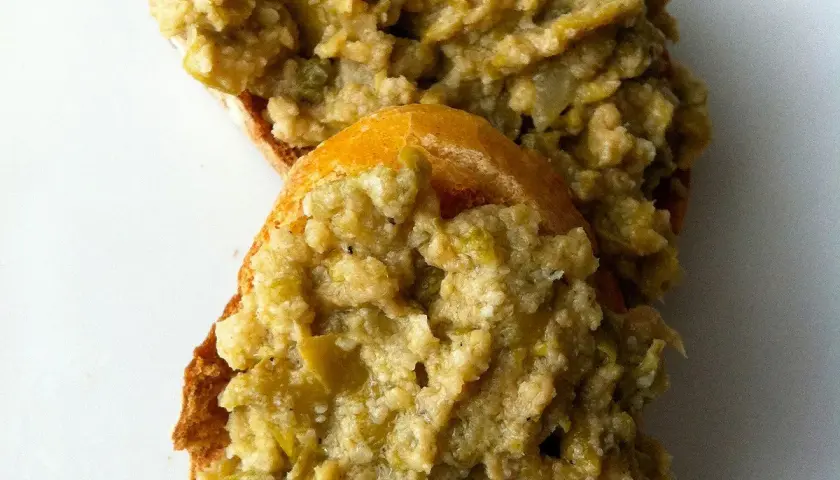 Deux tranches de pain garnies d'une généreuse portion de tapenade verte, prêtes à être dégustées.