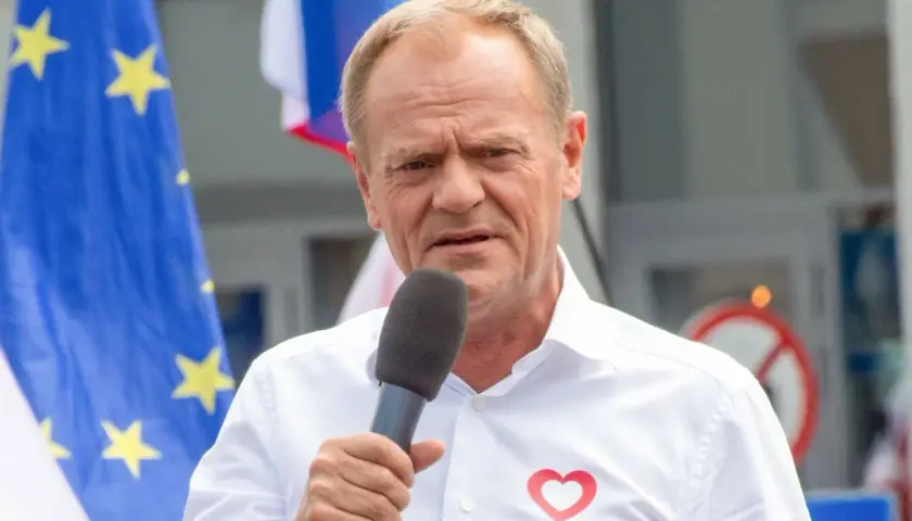 Donald Tusk przemawia w Ostródzie, z flagą UE i sercem na koszuli.