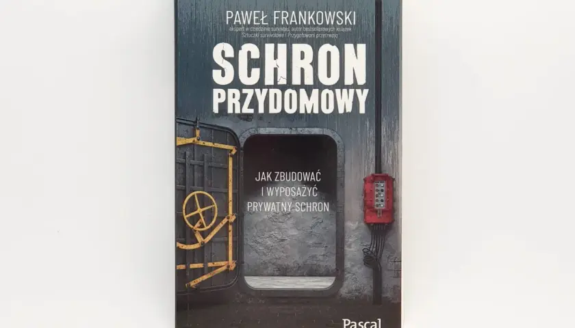 Okładka książki "Schron przydomowy" Pawła Frankowskiego. Przedstawia wejście do schronu z żółtą kierownicą i czerwoną skrzynką elektryczną.