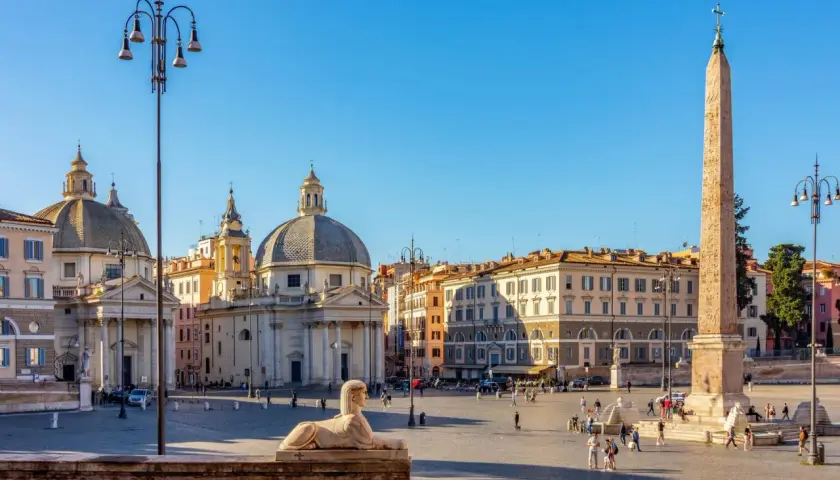 La Piazza del Popolo à Rome, avec ses églises jumelles, son obélisque et son sphinx, sous un ciel bleu éclatant.
