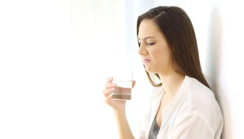 Donna con espressione disgustata tiene un bicchiere d'acqua, avvertendo un sapore metallico in bocca.