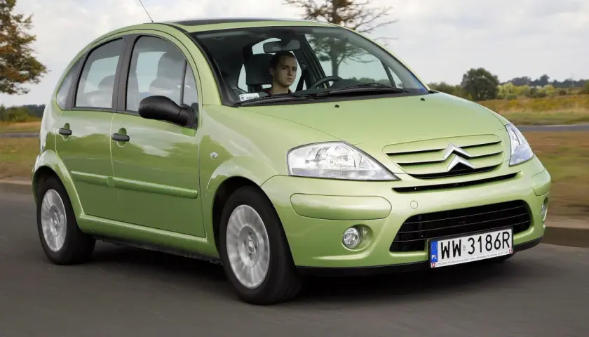 Zielony Citroen C3 2005 z młodym kierowcą za kierownicą przemierza wiejską drogę.