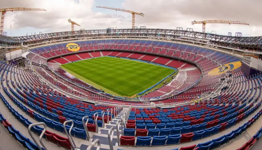 Stadion de la Cartuja w budowie, z widocznymi dźwigami i pustymi trybunami w kolorach czerwonym i niebieskim.