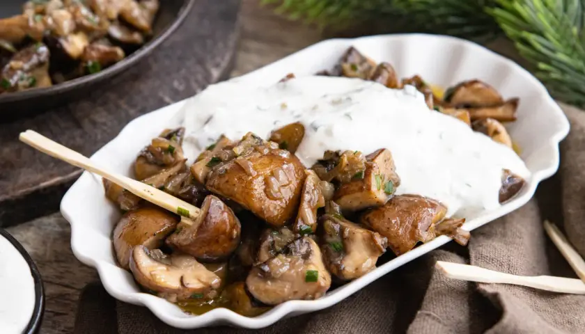 Gebratene Champignons mit Kräuterquark, wie vom Weihnachtsmarkt, auf einem weißen Teller mit Holzspießen.