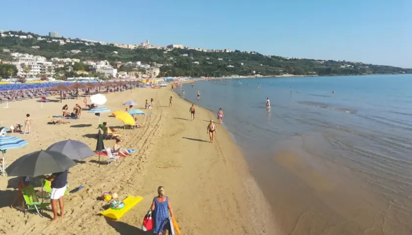 Plage animée à Vasto, Italie, avec des parasols colorés, des baigneurs et une ville en arrière-plan.