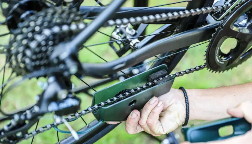 Czyszczenie łańcucha rowerowego za pomocą specjalnego narzędzia. Widać mechanizm przerzutek i zębatki.