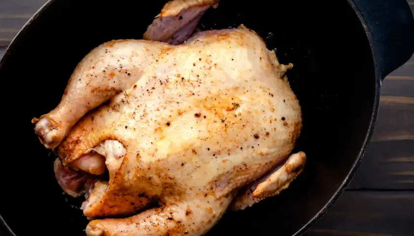 Un poulet rôti doré, assaisonné de poivre, repose dans une cocotte en fonte. Un délice prêt à être dégusté, un vrai poulet Calvi.