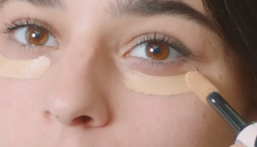 Aplicando corrector para disimular las ojeras antes o después del maquillaje.