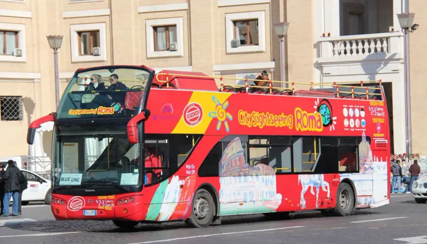 Un bus rouge à deux étages, un bus touristique "City Sightseeing Roma", circule dans la ville.