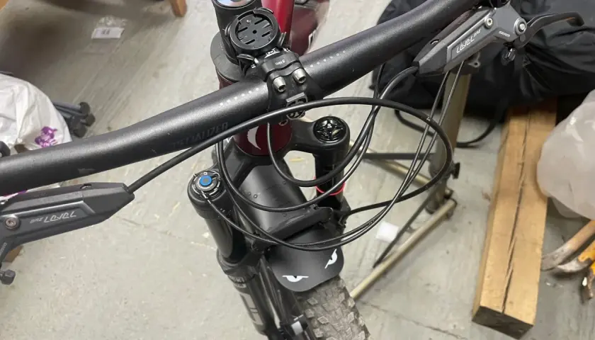 Close-up of a mountain bike's handlebars and front fork, showing the brake levers and the neat routing of the cutting hydraulic hose.