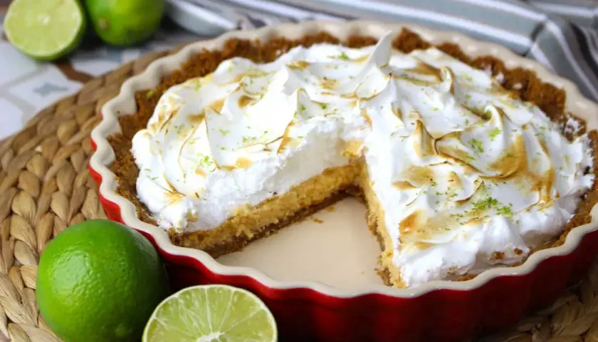 Delicioso key lime pie con merengue dorado y ralladura de lima, acompañado de limas frescas.
