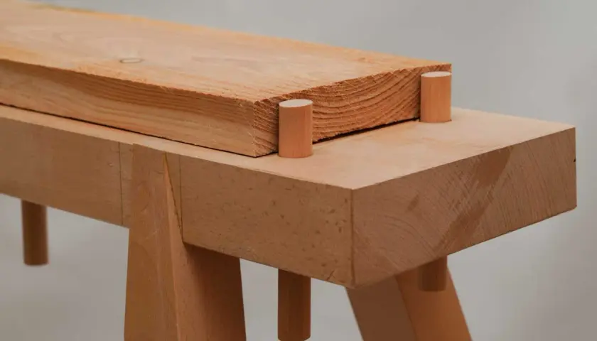 Holzverbindung für eine Werkbank selbst bauen: Ein Holzbalken ruht auf zwei Holzdübeln, die in einer weiteren Holzplatte stecken.