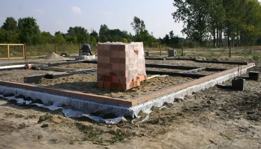 Rozpoczęcie budowy domu: wykopy pod fundamenty, ułożone bloczki i paleta cegieł.