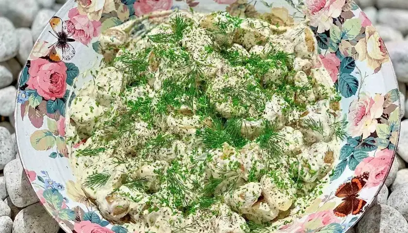 En stor skål med krämig potatissallad, toppad med dill och gräslök. Den vackra skålen har ett blommönster med fjärilar. Detta är nog den godaste potatissalladen!