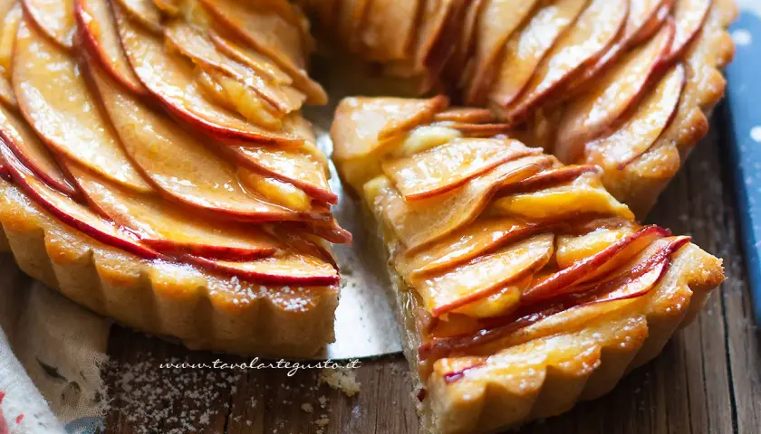Una deliziosa crostata di mele, con le fette di mela disposte a rosa e lucide di glassa, su un tagliere di legno.