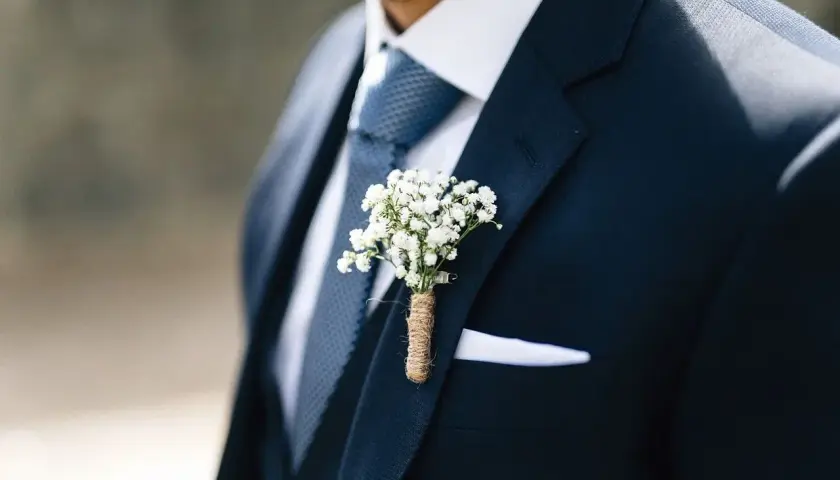 Elegancki granatowy garnitur z niebieskim krawatem, białą poszetką i bukiecikiem gipsówki.