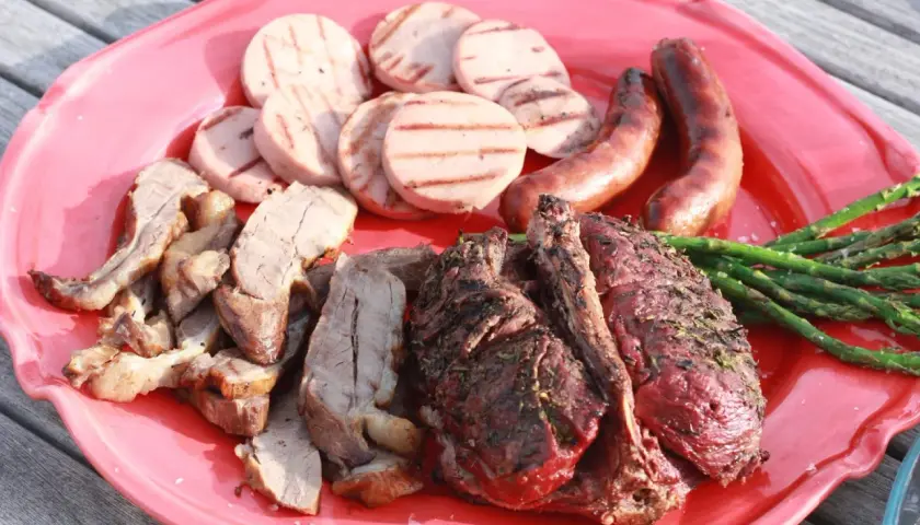 En stor röd bricka med grillad rådjur, korv, grillad korv och sparris. En härlig sommarmåltid!